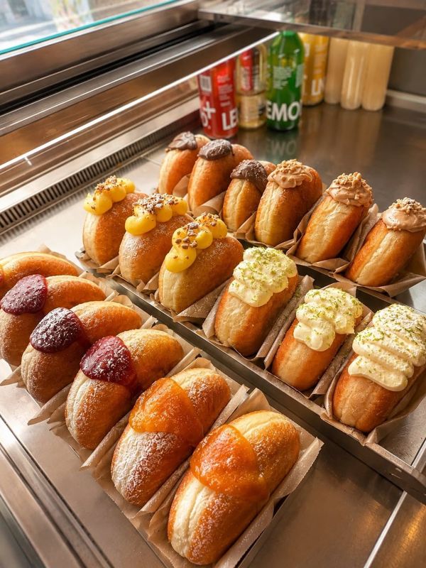 Une vitrine de beignets garnis alignés, crème pistache, citron et fruits rouges