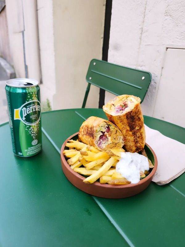 Un durum et ses frites sur une table de terrasse verte, à côté d’une canette