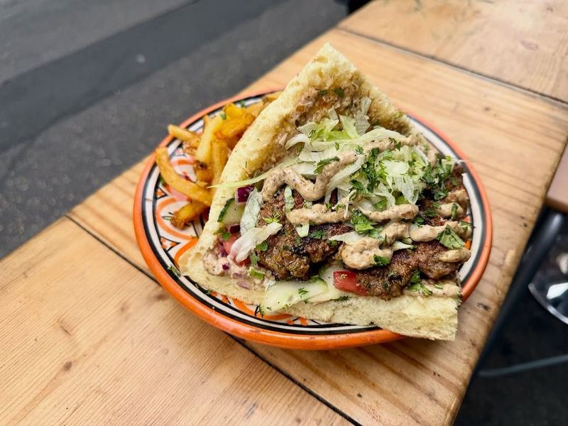 Un pain marocain garni de viande, de frites et de sauce, sur une assiette peinte