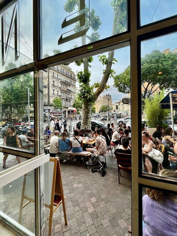La terrasse animée de la place Notre-Dame-du-Mont vue depuis l’intérieur de La Nena