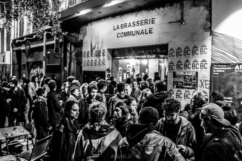 Une foule dense devant l'entrée de La Brasserie communale, en noir et blanc