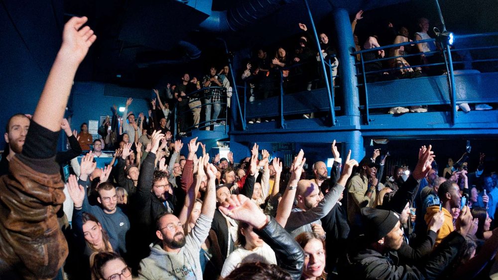 Une foule les bras levés devant la scène, sous la mezzanine bleue de l'Espace Julien