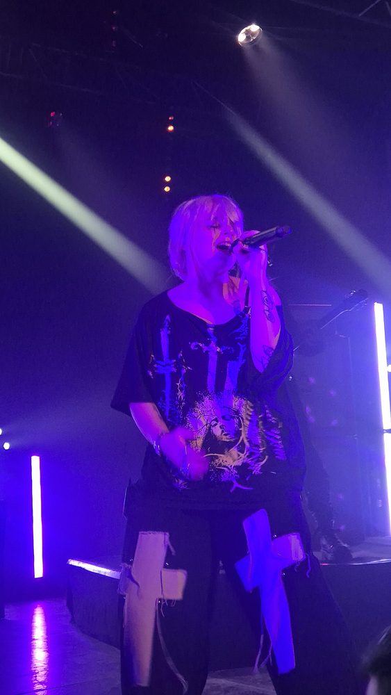 Une chanteuse aux cheveux blonds chante au micro sous les projecteurs bleus de l'Espace Julien