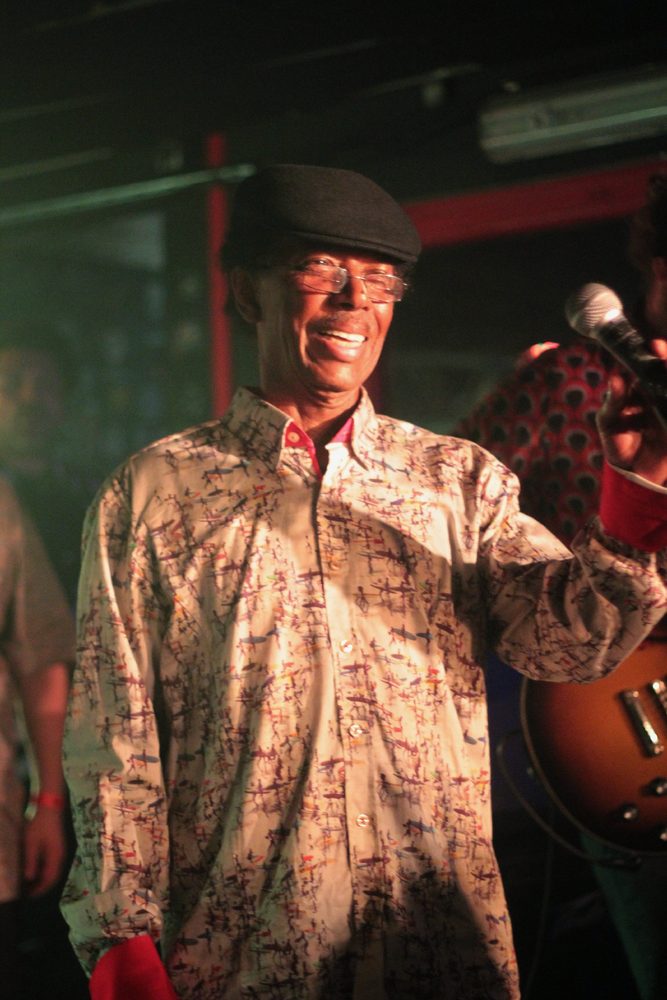 Un chanteur en chemise imprimée et casquette, sourire aux lèvres, sur la scène du Molotov